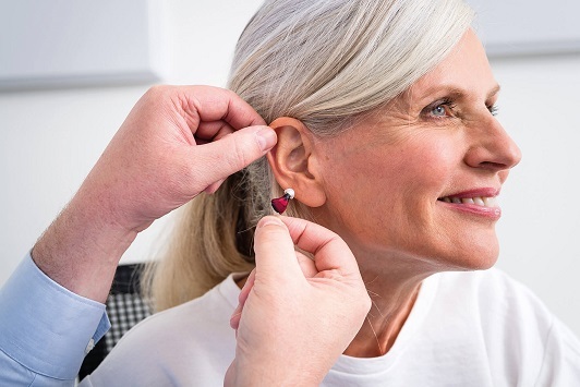 Eine Seniorin bekommt ein modernes Hörgerät vom Hörakustiker ins Ohr eingesetzt.